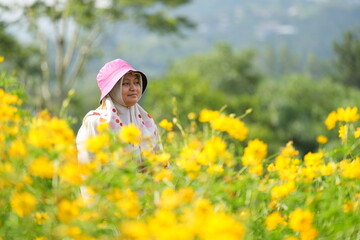 Fototapeta premium Portrait of Asian woman in a yellow flower garden and enjoying its beauty