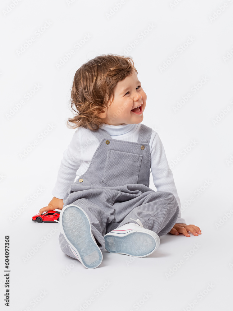 Wall mural a cheerful laughing caucasian toddler 2 years old with curly hair in a gray jumpsuit and a white tur