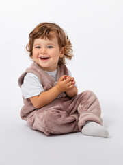 A happy cheerful little boy, a toddler of 1-2 years old, is sitting on the floor in a lilac plush suit, laughing and clapping his hands. Copy space. Photo.