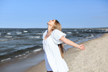 Fototapeta na wymiar Happy smiling beautiful woman is on the ocean beach in a white summer dress, open arms.
