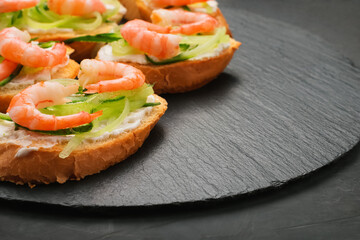 Sandwiches with shrimp, cheese and cucumber close-up on a black slate stand. Horizontal photo.