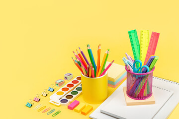 School stationery, pencils, rulers, paints, paper clips, notepad, sharpeners, scissors, notebook on a yellow background. Copy Space