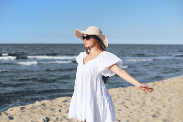 Happy blonde woman is on the ocean beach in a white dress and sunglasses, open arms.