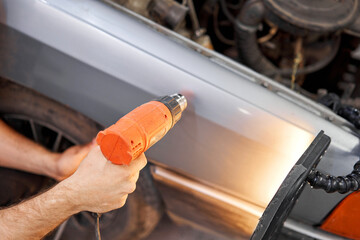 Car service worker warms car with heat gun. Removing dents on the car. PDR technology. Car body repair without painting.