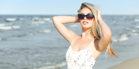 Happy blonde woman in free happiness bliss on ocean beach standing with sun glasses