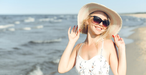 Happy blonde woman in free happiness bliss on ocean beach standing with sun glasses and hat.