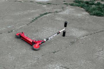 The red scooter lies on the pavement. Abandoned red scooter