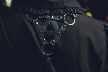Back shot of a lady with curly hair in a white sleeveless blouse and a black harness made of...