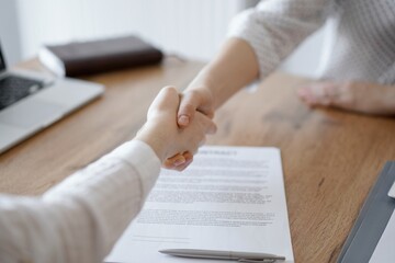 Business people shaking hands above contract papers just signed on the wooden table, close up. Lawyers at meeting. Teamwork, partnership, success concept.