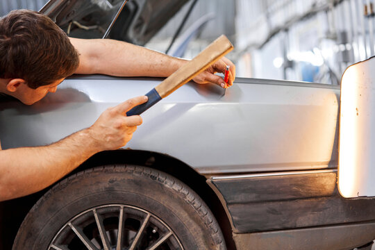A car service worker knocks with a hammer. Removing dents on the car. PDR technology. Car body repair without painting.