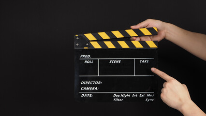 Obraz premium Hand's holding and point at yellow and black Clapper board on black background.