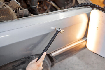 A car service worker knocks with a hammer. Removing dents on the car. PDR technology. Car body...