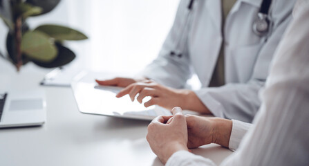 Doctor and patient discussing current health examination while sitting at the desk in clinic office. The focus is on female patient's hands, close up. Perfect medical service and medicine concept.