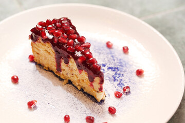 A piece of cheesecake decorated with pomegranate seeds, on a white plate, selective focus, top view.