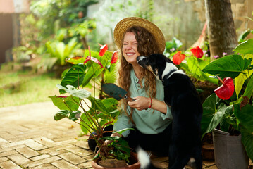 Young woman cuddling and snuggling with her pet dog laughing. Caucasian female gardener with trowel...