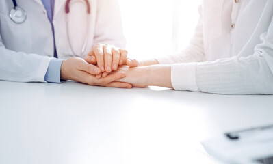 Doctor and patient sitting near each other at the table in clinic office. The focus is on female physician's hands reassuring woman, only hands, close up. Medicine concept.