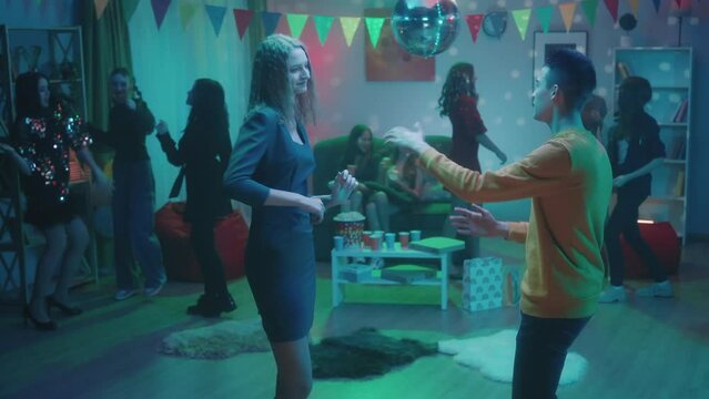 At the party, teenagers dance in separate groups. The guy dances with the girl away from everyone. The guy flirts with the girl close up. Party, birthday, celebration.
