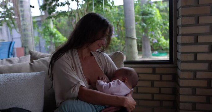 Mother breastfeeds infant baby girl in house during summer