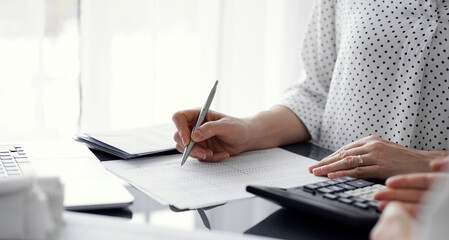 Woman accountant using a calculator and laptop computer while counting and discussing taxes with a...
