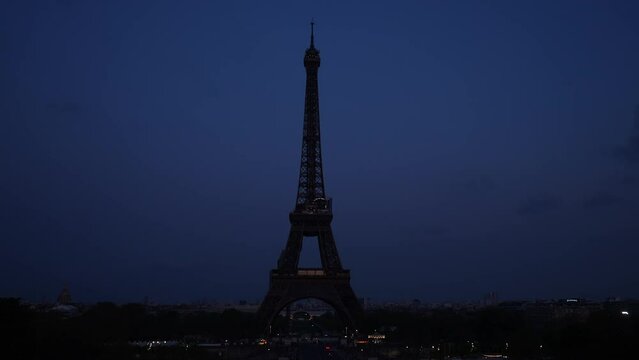 Remote silhouette of the Eiffel Tower without lighting against dark sky. Iconic symbol of Paris, famous historical landmark in France. Concept of vacations in France. Shooting in slow motion.
