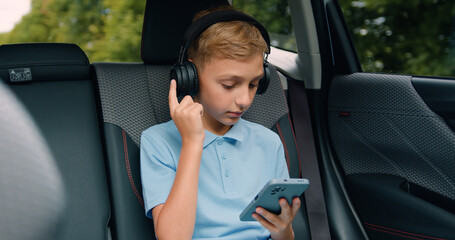 Teen boy playing game with digital tablet and celebrate victory while sitting in the back seat of carchild travelling in automobile.
