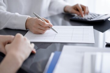 Woman accountant using a calculator and laptop computer while counting taxes for a client. Business audit concepts.