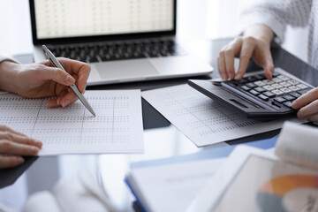 Woman accountant using a calculator and laptop computer while counting taxes for a client. Business audit concepts.