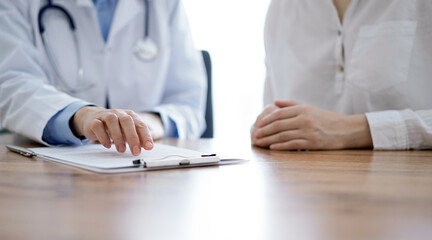 Doctor and patient  discussing something while sitting near each other at the wooden desk in clinic. Medicine concept.