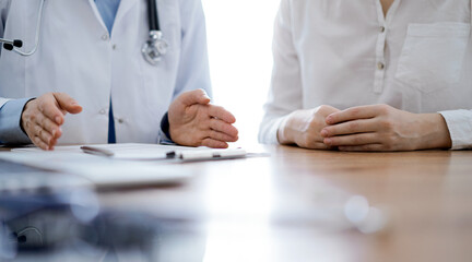 Doctor and patient  discussing something while sitting near each other at the wooden desk in clinic. Medicine concept.