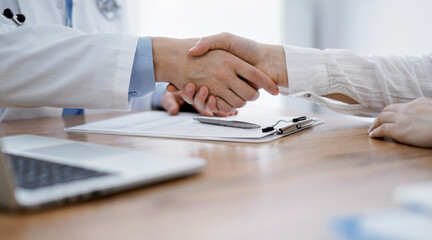 Doctor and patient shaking hands above the wooden table in clinic. Medicine concept.