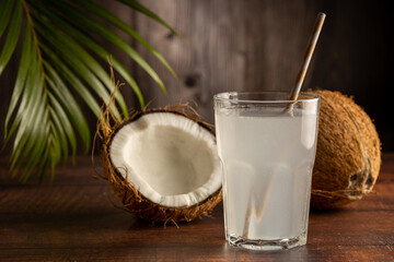 Glass with fresh coconut water and coconuts on the table.