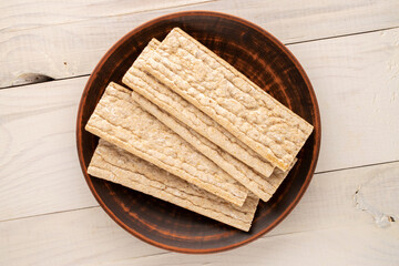 Several rye crispbreads with a clay plate on a wooden table, close-up, top view.