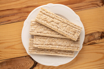 Several rye crispbreads with a white plate on a wooden table, close-up, top view.