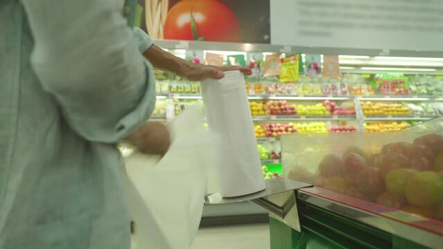 Man buyer tear off a plastic bag in a supermarket against the background of a vegetables and fruits shop 4K
