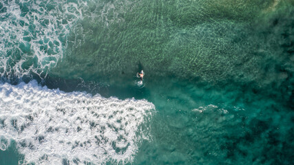 Aerial view of a wave in the ocean with surfers nearby