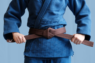Judo girl with brown belt. A judoka teenager fighter poses in a blue kimono on a plain background....