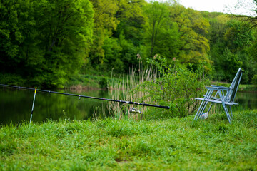 Fisherman's chair and fishing rod in the background over the lake at dawn. Fishing concept. Beautiful sunrise - morning landscape. Place of a fisherman with a fishing rod in the fog