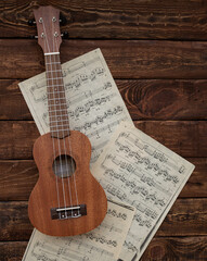 Ukulele guitar on music sheets on wooden background