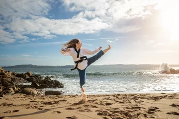 Fotobehang Beachside Warrior: Capturing the Skill and Determination of a Young Woman's Taekwondo Kick © larrui