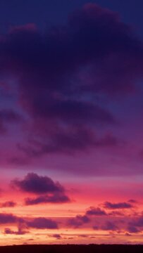 Fiery dawn and rare cumulus clouds in the blue and red sky. Timelapse video. Vertical video. Dramatic fiery sunset with orange and red clouds