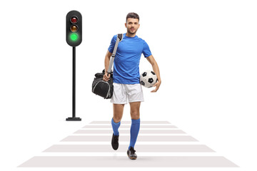 Full length portrait of a soccer player with a bag and a football crossing street