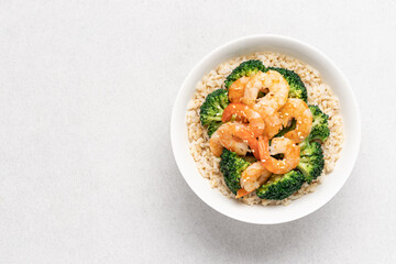 Rice with broccoli and fried shrimp in white bowl on light background with copy space. Healthy food with vegetables and seafood