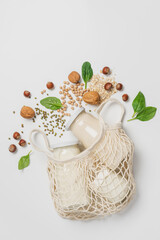 Variety of vegan plant based milk in zero waste mesh bag. Top view of lactose free milk based on nuts, legumes, oatmeal on white background