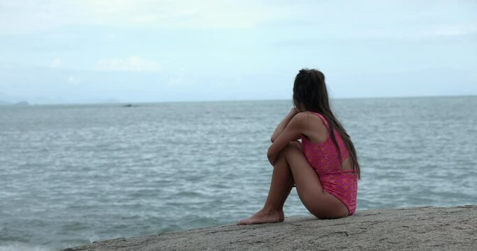 Woman sitting on rocks looking off into ocean - looking sad