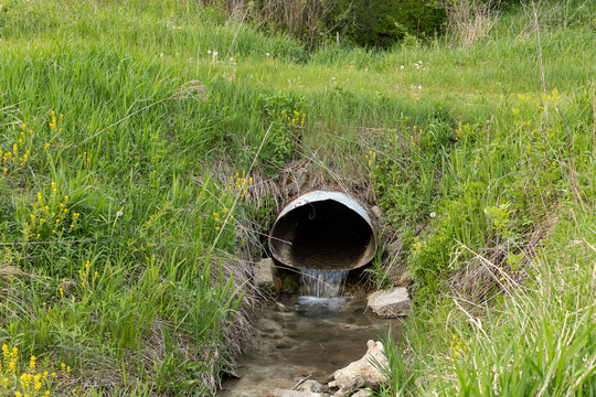A large culvert in a ditch with clear water flowing through it. 