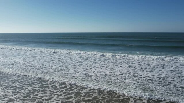 view from a drone in motion on the waves zooming in to open its viewing angle from the beach