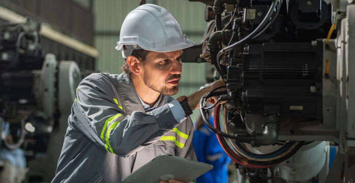 male automation engineer in uniform helmet safety inspection check control heavy machine robot arm system in industrial factory. technician worker check for repair factory machine