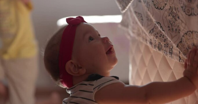 Cute baby girl learning to lift herself into a stand on parents bed - close up on face
