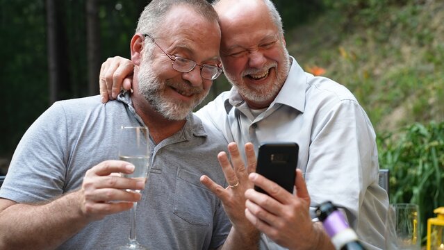 Two gay men have video chat on phone with friends showing their engagement ring for their marriage.