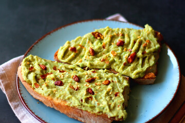 Turquoise plate with two pieces of avocado toast on dark background. Selective focus.